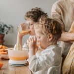 A loving family moment with children drinking fresh orange juice indoors.